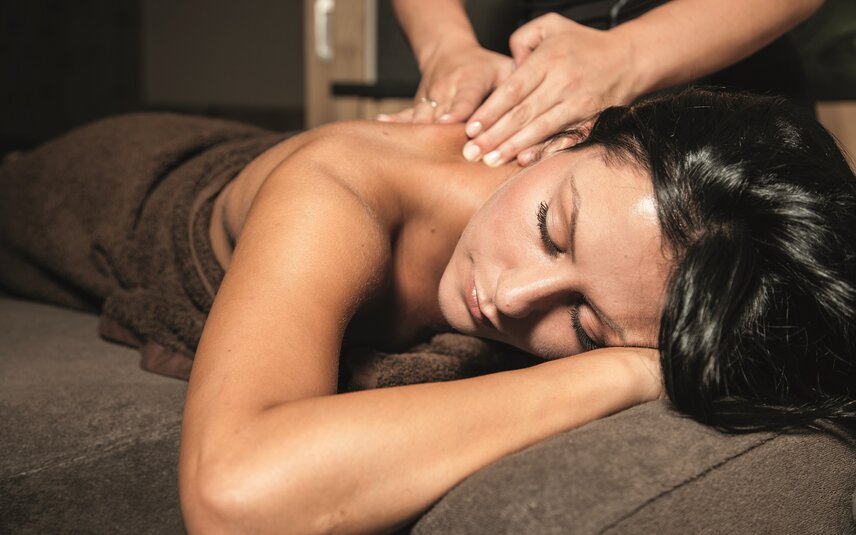 Eine dunkelhaarige Frau liegt auf einer Massageliege und bekommt eine Rückenmassage | © Silvretta Montafon