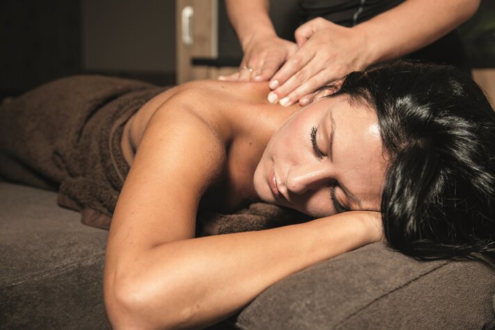 Eine dunkelhaarige Frau liegt auf einer Massageliege und bekommt eine Rückenmassage | © Silvretta Montafon