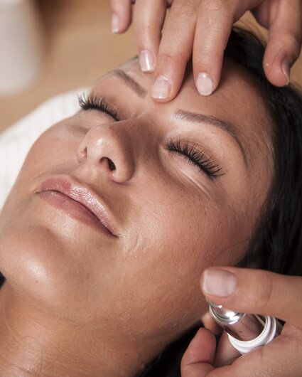 Eine dunkelhaarige Frau bekommt eine Gesichtsmassage | © Silvretta Montafon