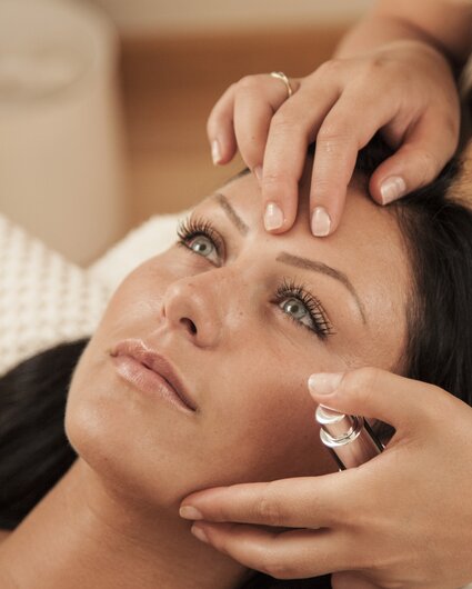 Eine dunkelhaarige Frau bekommt eine Gesichtsmassage von einer Masseurin | © Silvretta Montafon