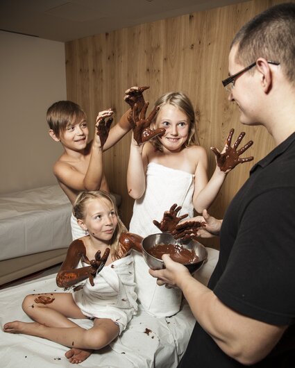 Drei Kinder bekommen eine Schokolademassage und haben die Hände voll mit Schokolade  | © Silvretta Montafon
