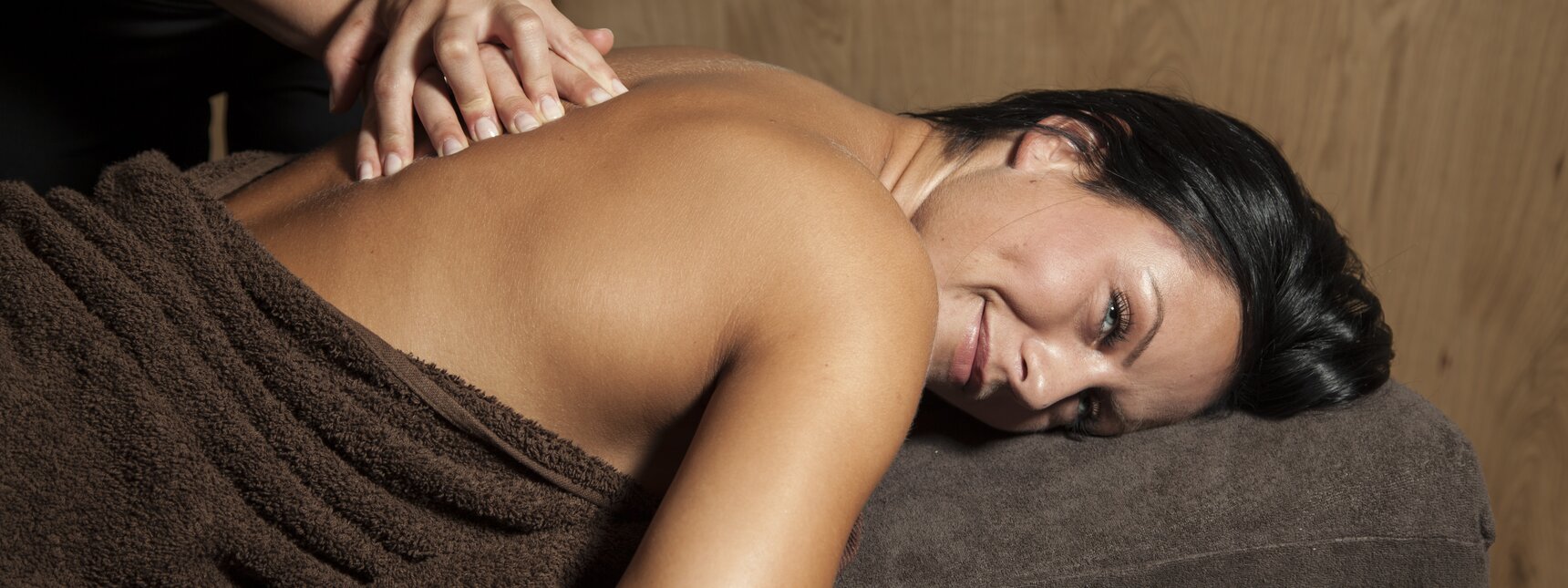 Eine dunkelhaarige Frau liegt auf einer Massageliege und bekommt eine Rückenmassage | © Silvretta Montafon