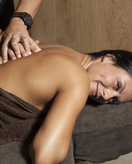 Eine dunkelhaarige Frau liegt auf einer Massageliege und bekommt eine Rückenmassage | © Silvretta Montafon
