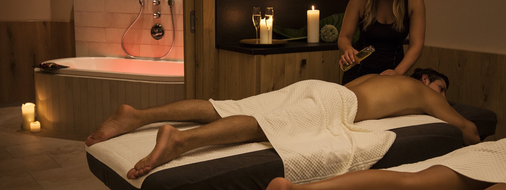 Eine blonde Frau massiert eine Brünette bei einer Partnermassage und gießt ihr Öl auf den Rücken | © Silvretta Montafon 