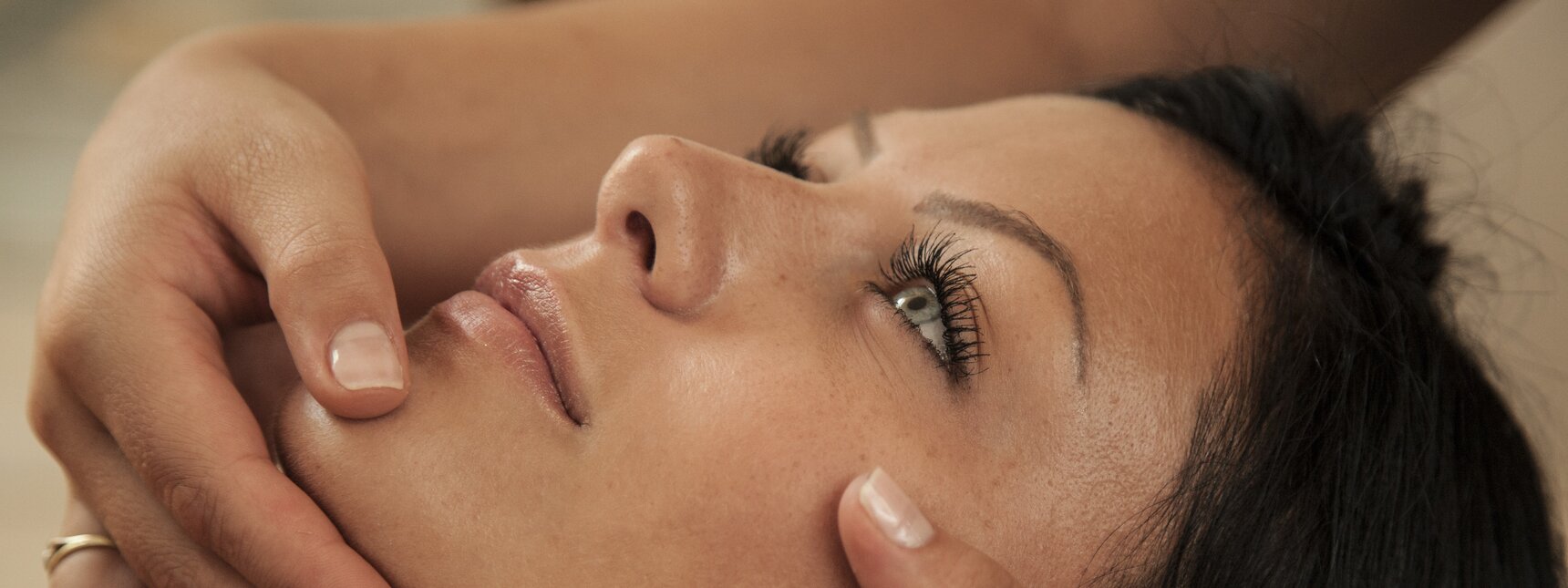 Eine dunkelhaarige Frau bekommt eine Gesichtsmassage von einer Masseurin | © Silvretta Montafon