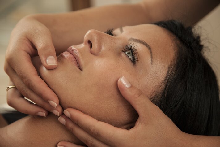 Eine dunkelhaarige Frau bekommt eine Gesichtsmassage von einer Masseurin | © Silvretta Montafon