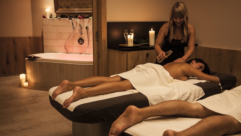 Eine blonde Frau massiert eine Brünette bei einer Partnermassage und gießt ihr Öl auf den Rücken | © Silvretta Montafon