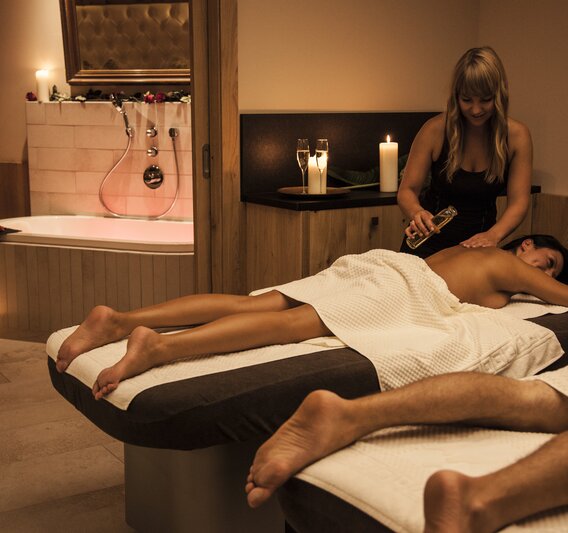 Eine blonde Frau massiert eine Brünette bei einer Partnermassage und gießt ihr Öl auf den Rücken | © Silvretta Montafon