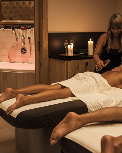 Eine blonde Frau massiert eine Brünette bei einer Partnermassage und gießt ihr Öl auf den Rücken | © Silvretta Montafon