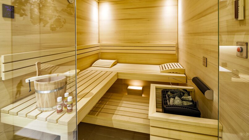 Eine Sauna mit zwei Liegen udn einer Sitzfläche und einem Aufgusskübel sowie den heißen Steinen | © Silvretta Montafon