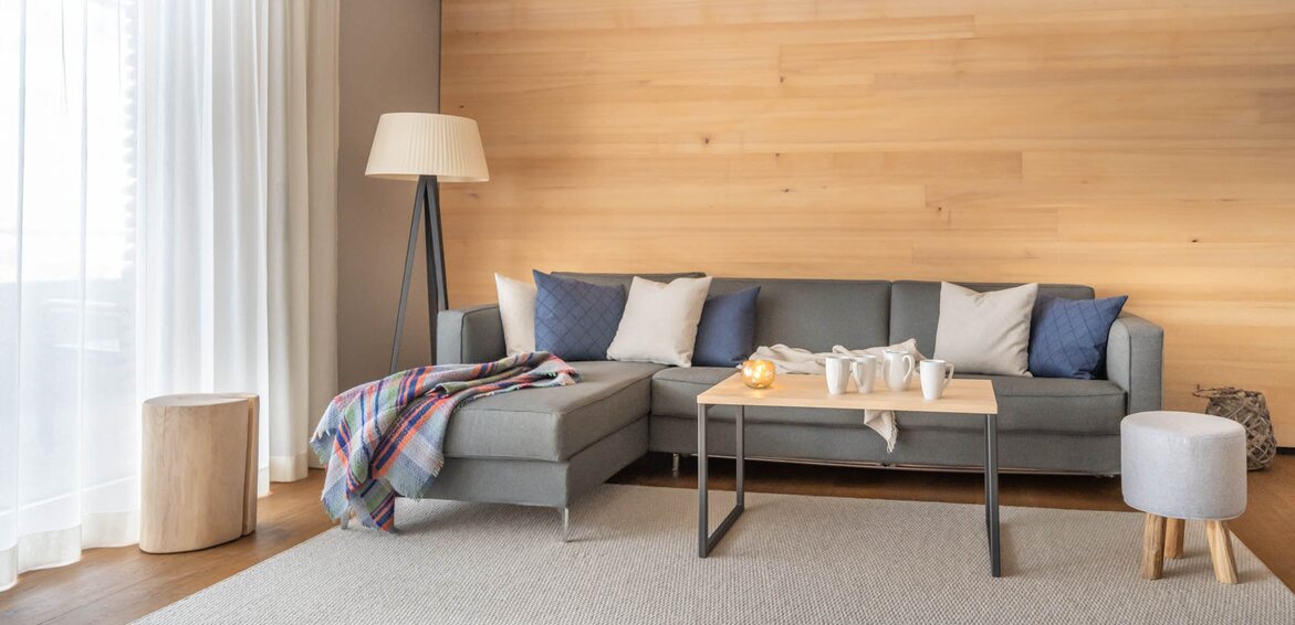Sporthotel Chalet Silvretta Montafon | © Silvretta Montafon - blateral Eine große graue Couch auf einem hellgrauen Teppich und einem Mensch Ärger Dich Nicht Spiel im Vordergrund | © Silvretta Montafon - blateral
