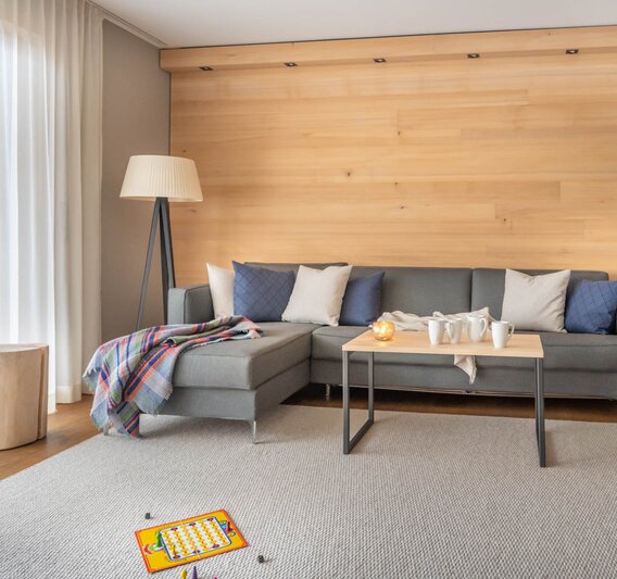 Eine große graue Couch auf einem hellgrauen Teppich und einem Mensch Ärger Dich Nicht Spiel im Vordergrund | © Silvretta Montafon - blateral