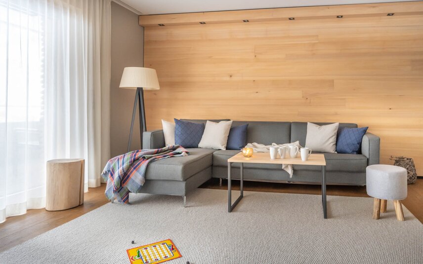 Eine große graue Couch auf einem hellgrauen Teppich und einem Mensch Ärger Dich Nicht Spiel im Vordergrund | © Silvretta Montafon - blateral