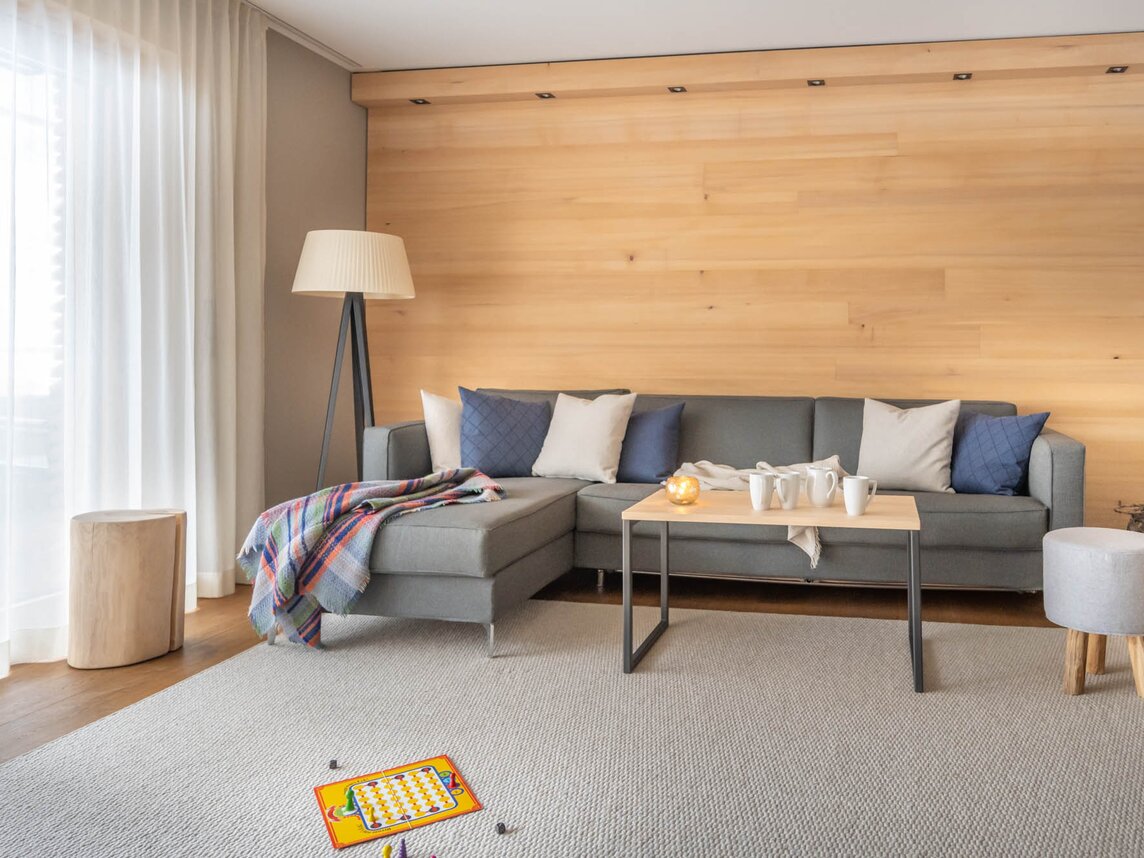 Eine große graue Couch auf einem hellgrauen Teppich und einem Mensch Ärger Dich Nicht Spiel im Vordergrund | © Silvretta Montafon - blateral