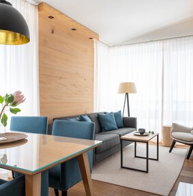 Ein gemütlicher Wohnessbereich mit einer grauen Couch und einem Holzesstisch | © Silvretta Montafon - blateral