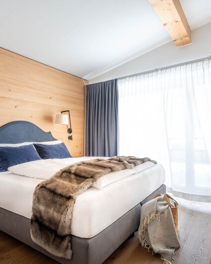 Ein gemütliches großes Bett mit grauer Polsterung und einer Felldecke darüber | © Silvretta Montafon - blateral