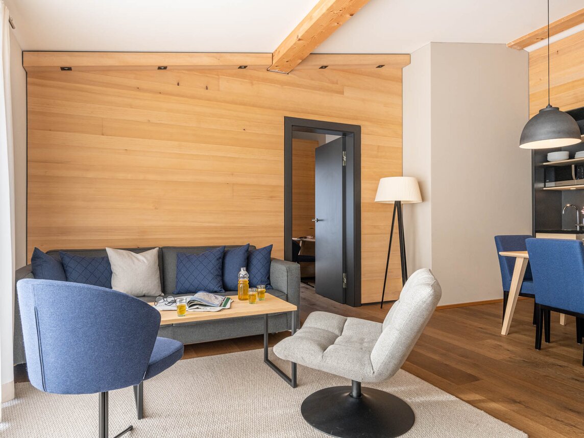 Ein gemütlicher Wohnbereich mit einer blauen Couch, einem blauen Sessel und einem hellgrauen Drehstuhl | © Silvretta Montafon - blateral