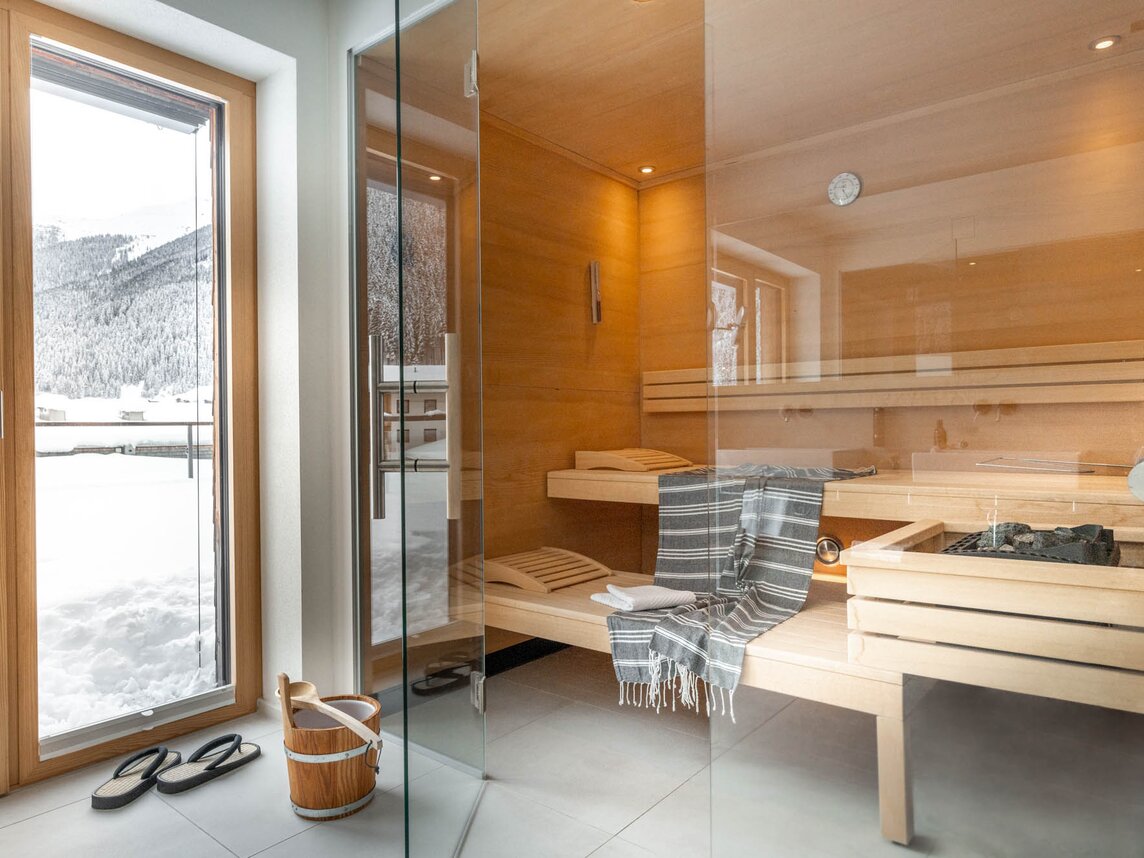 Eine gemütliche Sauna mit drei Liegen und einer Glaswand mit Pantoffeln davor | © Silvretta Montafon - blateral