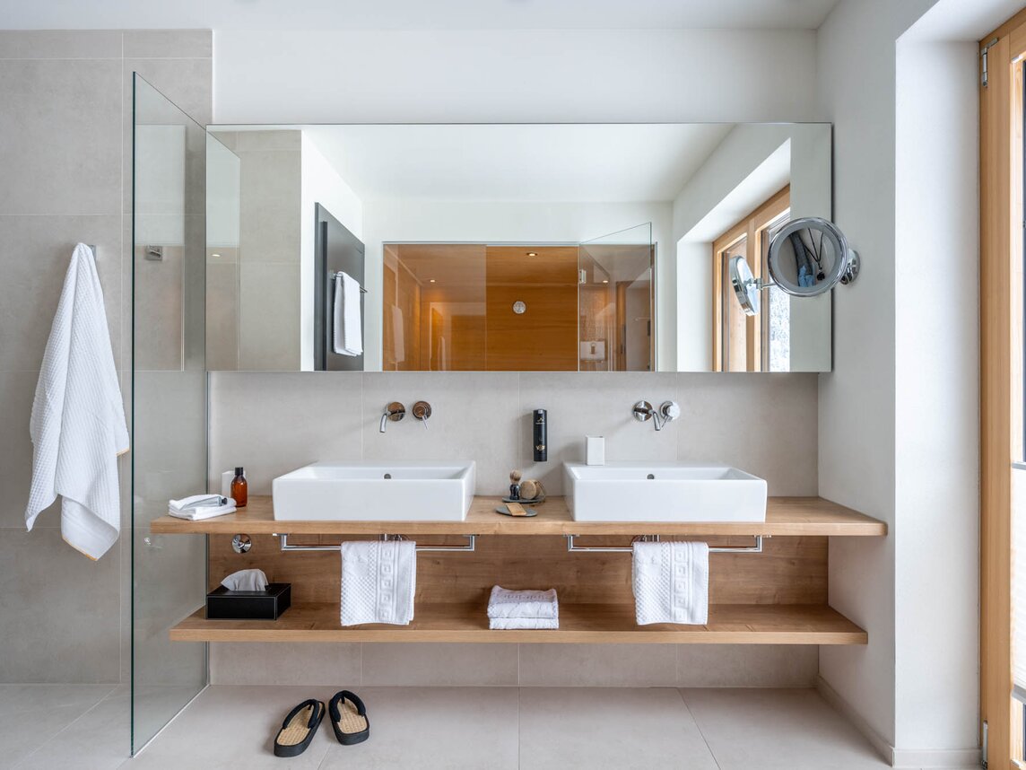 Ein Waschtisch aus Holz mit zwei Waschbecken und eine Dusche mit Duschglas  | ©  Silvretta Montafon - blateral