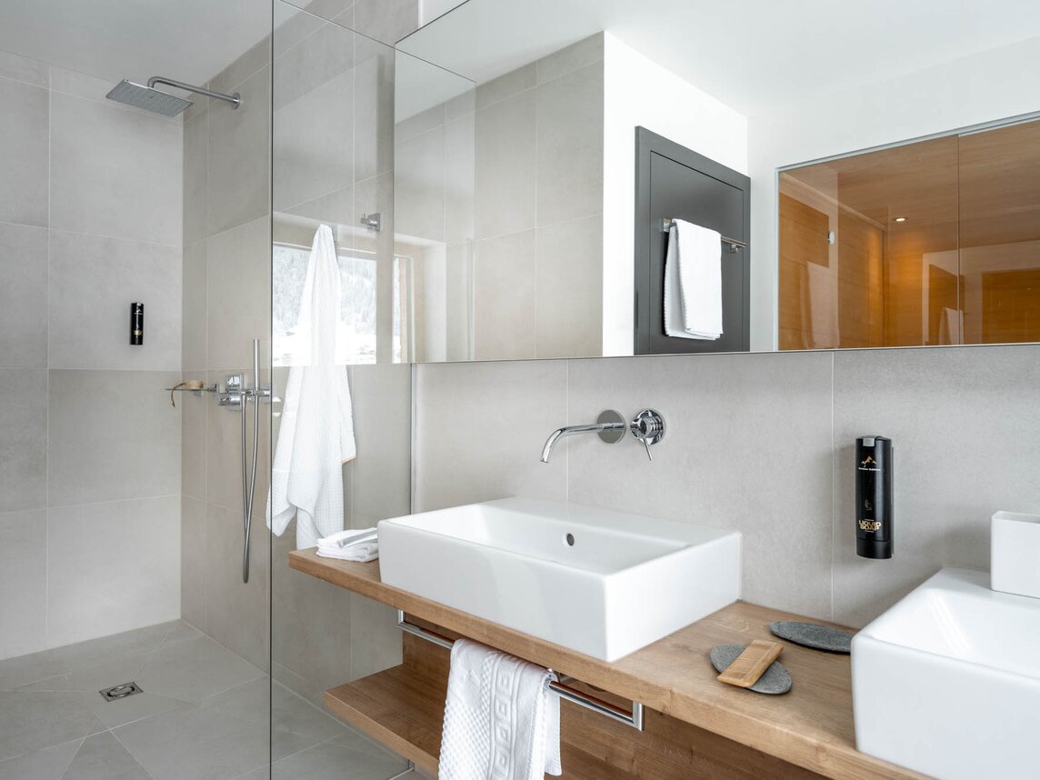 Ein Waschtisch aus Holz mit zwei Waschbecken und eine Dusche mit Duschglas  | © Silvretta Montafon - blateral