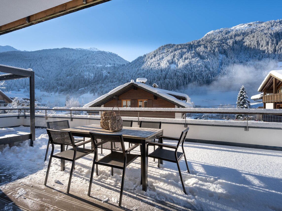 Ein Tisch mit Stühlen auf der verschneiten Terrasse mit einem Ausblick auf die schneebedeckten Berge | © Silvretta Montafon - blateral