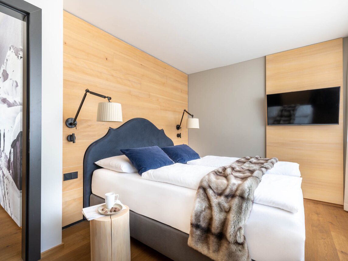 Ein gemütliches Bett mit grauer Polsterung, weißem Bettbezug und einer Felldecke | © Silvretta Montafon - blateral