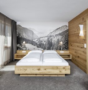 Gemütliches Doppelbett aus Holz mit einem schwarz weiß Bild von einem Bergpanorama | © Silvretta Montafon - Markus Gmeiner