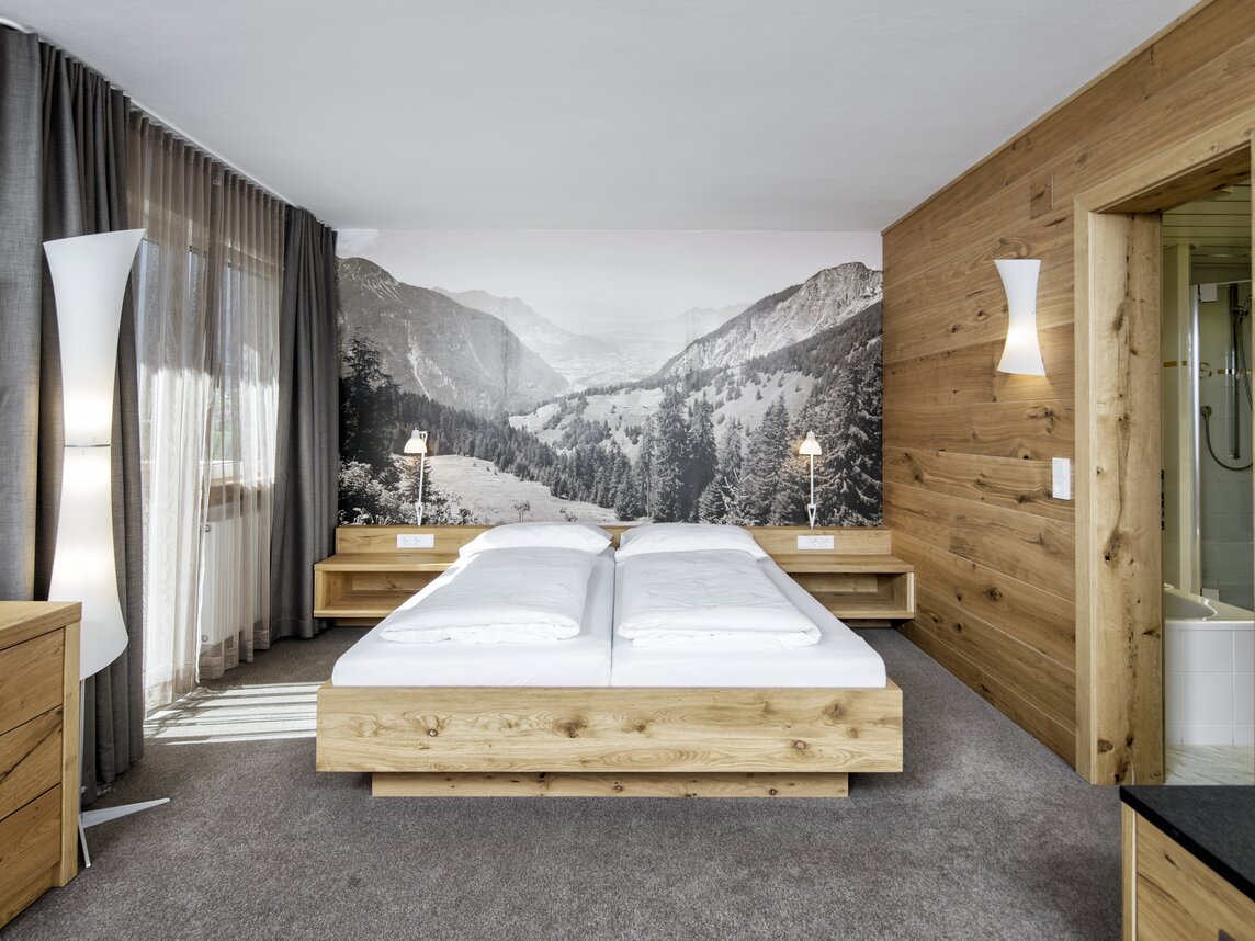 Gemütliches Doppelbett aus Holz mit einem schwarz weiß Bild von einem Bergpanorama | © Silvretta Montafon - Markus Gmeiner