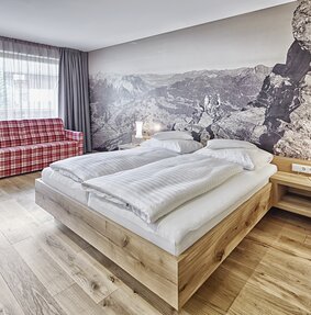 Gemütliche Junior Suite mit Doppelbett und kariertem Sofa | © Silvretta Montafon - Markus Gmeiner