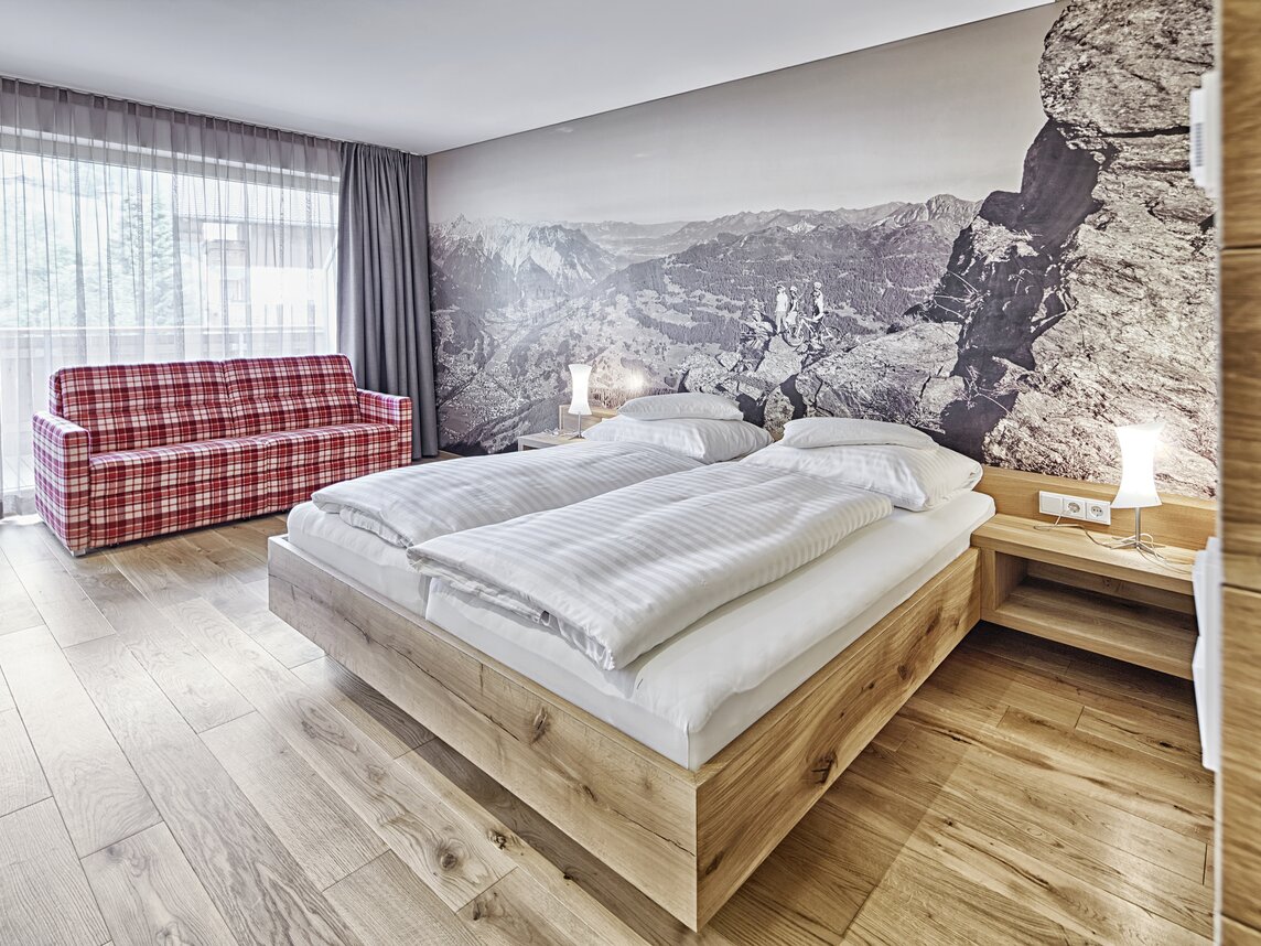 Gemütliche Junior Suite mit Doppelbett und kariertem Sofa | © Silvretta Montafon - Markus Gmeiner