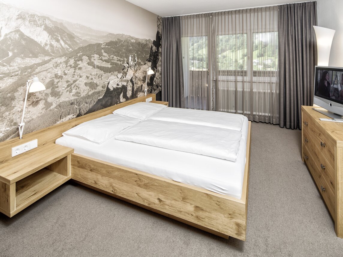 Gemütliche Bergsuite mit Doppelbett, Fernseher und Balkon im Sporthotel Silvretta Montafon | © Silvretta Montafon - Markus Gmeiner