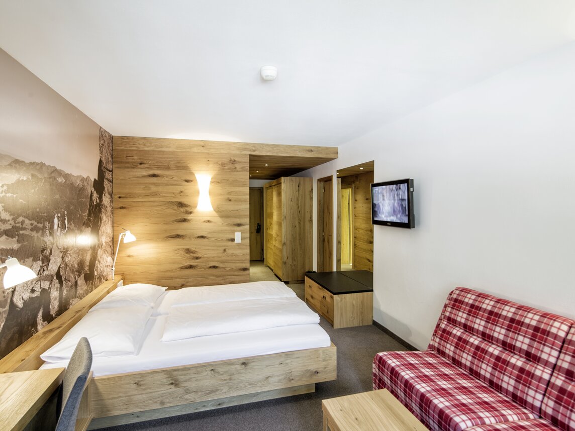 Gemütliches Doppelzimmer mit Sofa, Fernseher und großem Spiegel | © Silvretta Montafon - Markus Gmeiner
