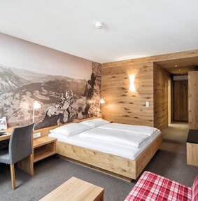 Doppelbett mit großem Schreibtisch und riesigem Wandposter | © Silvretta Montafon - Markus Gmeiner