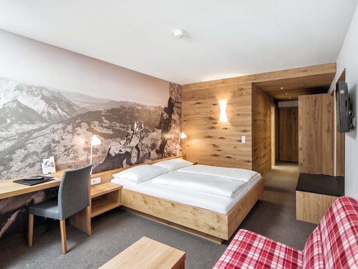 Komfortzimmer Sporthotel Silvretta Montafon  | © Silvretta Montafon - Markus Gmeiner Doppelbett mit großem Schreibtisch und riesigem Wandposter | © Silvretta Montafon - Markus Gmeiner