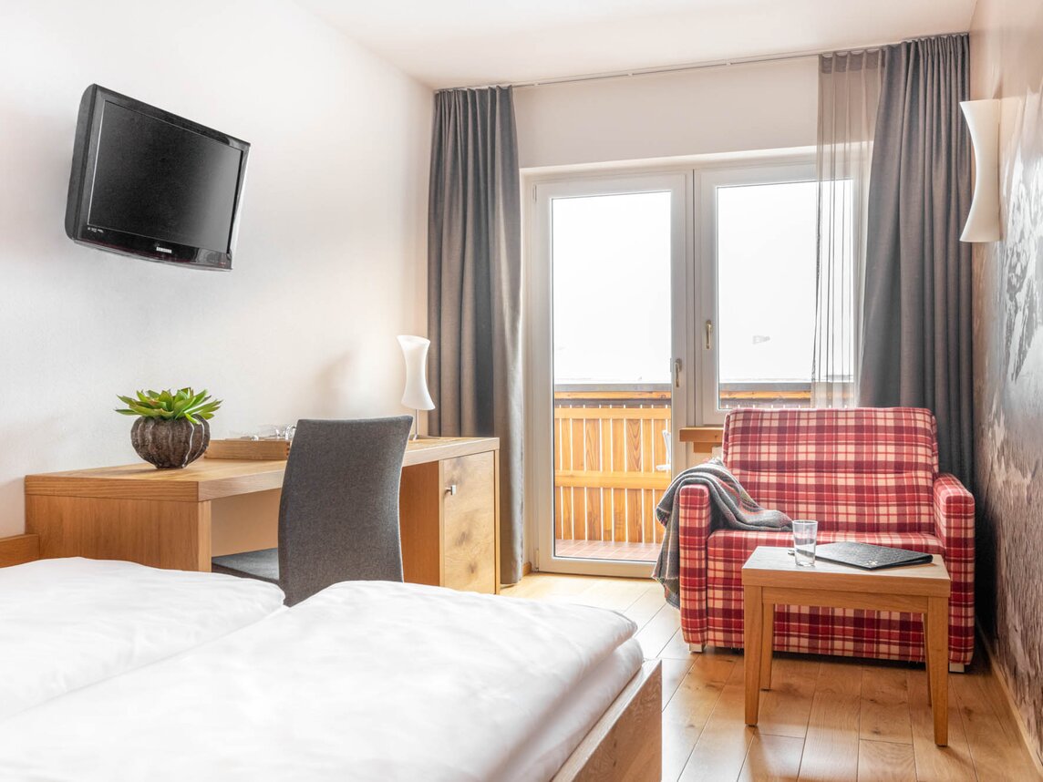 Ein kleiner Schreibtisch unter einem Fernseher an der Wand und ein rot-karierter Sessel | © Silvretta Montafon - blateral